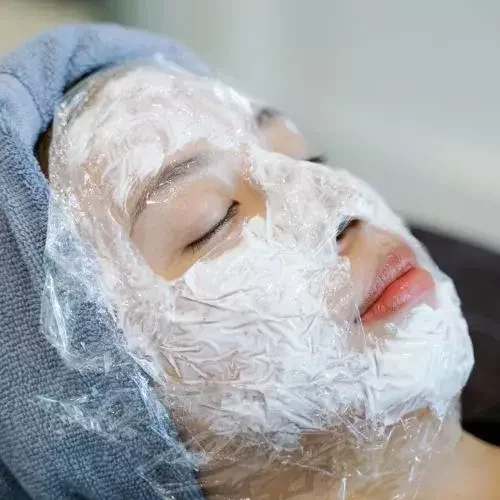 Patient lying down with numbing cream applied on her face, looking relaxed before the Korean laser treatment.