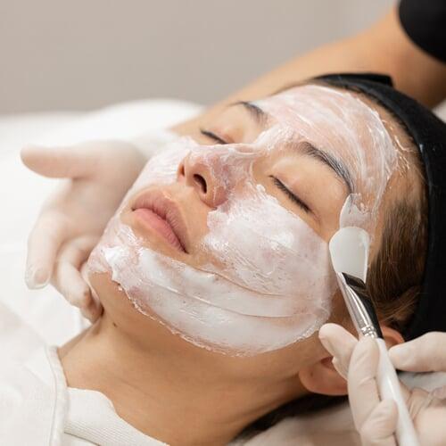 Patient lying down with numbing cream applied on her face, looking relaxed before the Korean laser treatment.